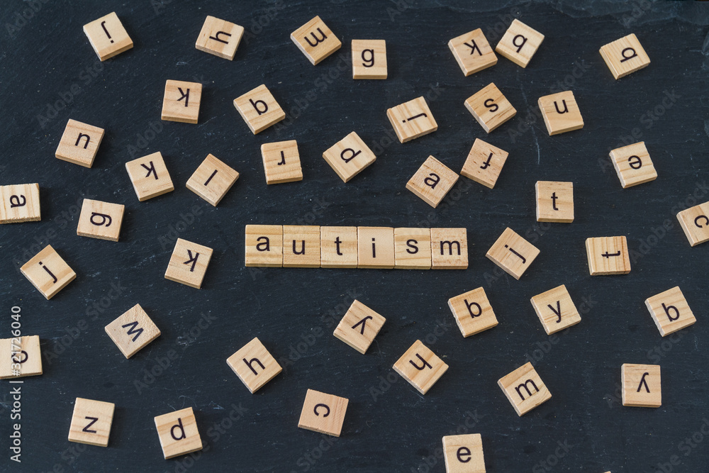 Autism spelled in wooden blocks, with lots of randomly spread letters.