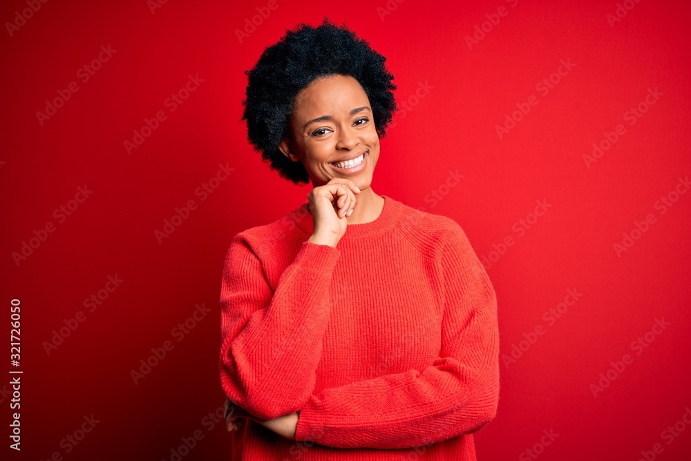 Young beautiful African American afro woman with curly hair wearing casual sweater looking confident at the camera with smile with crossed arms and hand raised on chin. Thinking positive. Young beautiful African American afro woman with curly hair wearing casual sweater looking confident at the camera with smile with crossed arms and hand raised on chin. Thinking positive.