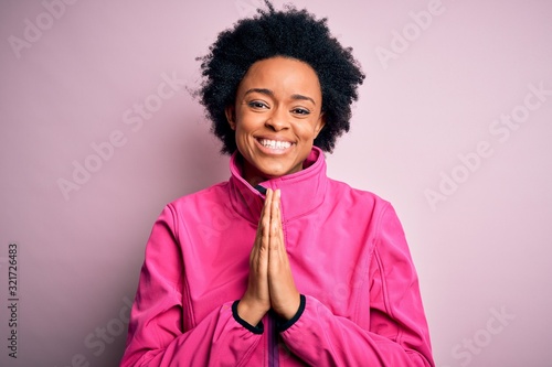Young African American afro sportswoman with curly hair wearing sportswear doin sport praying with hands together asking for forgiveness smiling confident.