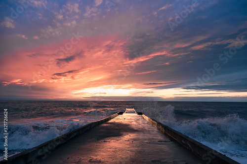 Big waves breaking on a stone pier in stormy weather with a bright sunset  a big tide. Black Sea. Sochi  February.