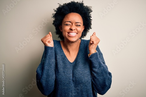 Young beautiful African American afro woman with curly hair wearing casual sweater excited for success with arms raised and eyes closed celebrating victory smiling. Winner concept.