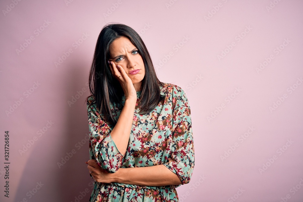 Young brunette woman with blue eyes wearing floral colorful dress over pink background thinking looking tired and bored with depression problems with crossed arms. Young brunette woman with blue eyes wearing floral colorful dress over pink background thinking looking tired and bored with depression problems with crossed arms.