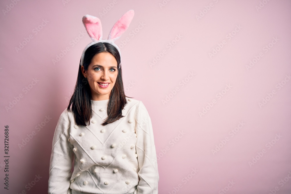 Young caucasian woman wearing cute easter rabbit ears over pink isolated background looking away to side with smile on face, natural expression. Laughing confident.