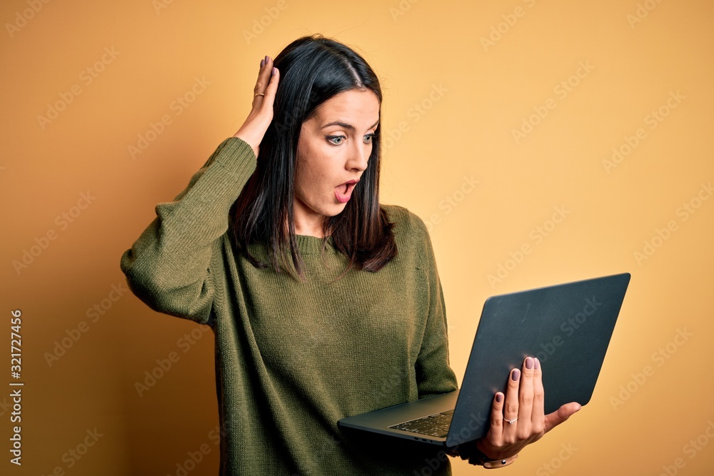 Young brunette woman with blue eyes working using computer laptop over yellow background Looking at the watch time worried, afraid of getting late Young brunette woman with blue eyes working using computer laptop over yellow background Looking at the watch time worried, afraid of getting late