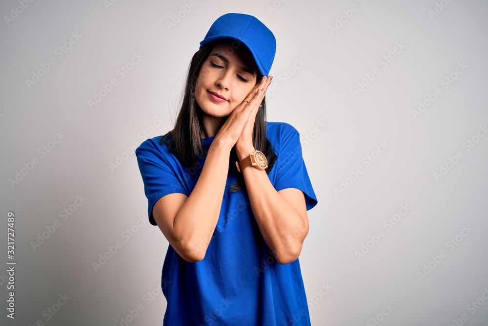 Young delivery woman with blue eyes wearing cap standing over blue background sleeping tired dreaming and posing with hands together while smiling with closed eyes. Young delivery woman with blue eyes wearing cap standing over blue background sleeping tired dreaming and posing with hands together while smiling with closed eyes.