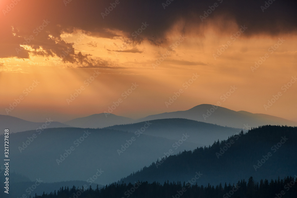 Majestic landscape of mountains at sunrise. View of the misty tops and layer hills of the mountains in the distance. Dramatic sky and rays of sunlight at morning. Concept of nature background.