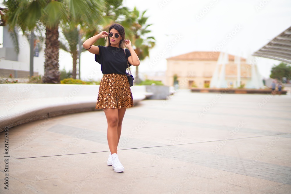 Young beautiful girl wearing sunglasses, t-shirt and animal print skirt walking at the park