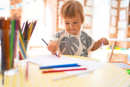 Adorable toddler drawing using paper and pencil around lots of toys at kindergarten