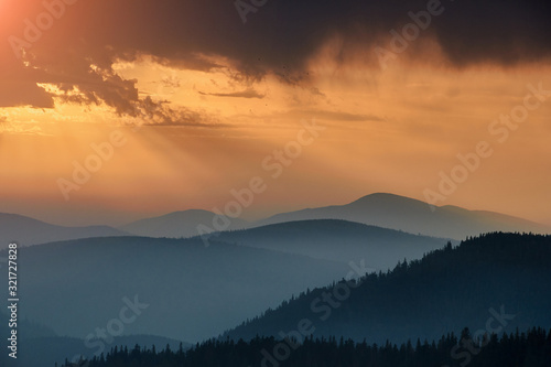 Fototapeta Naklejka Na Ścianę i Meble -  Majestic landscape of mountains at sunrise. View of the misty tops and layer hills of the mountains in the distance. Dramatic sky and rays of sunlight at morning. Concept of nature background.