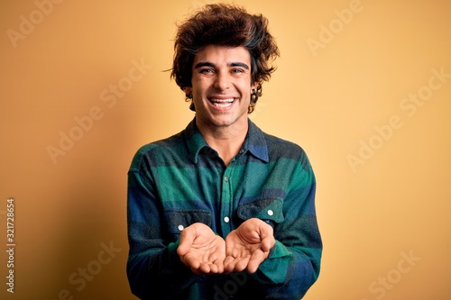 Young handsome man wearing casual shirt standing over isolated yellow background Smiling with hands palms together receiving or giving gesture. Hold and protection
