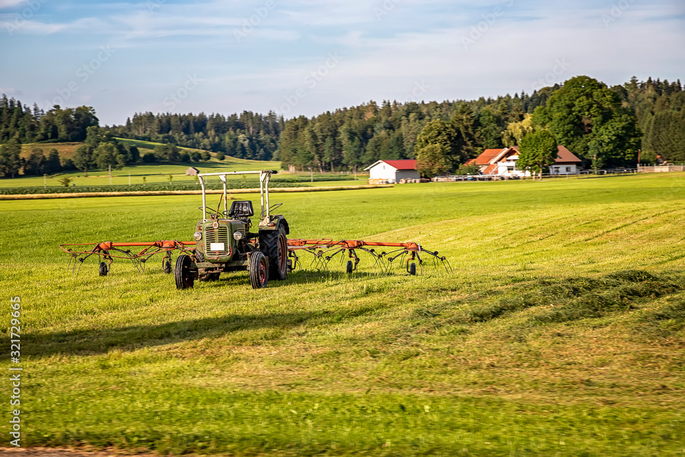The tractor and hay tedder prepare hay harvest for cultivation. Agriculture and agronomy concept. Selective focus The tractor and hay tedder prepare hay harvest for cultivation. Agriculture and agronomy concept. Selective focus