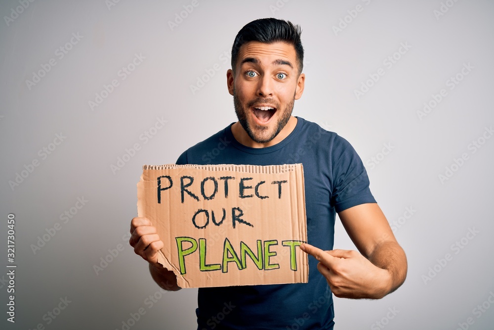Young handsome activist man protesting for the enviroment hoding cardboard very happy pointing with hand and finger Young handsome activist man protesting for the enviroment hoding cardboard very happy pointing with hand and finger