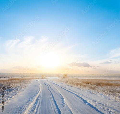 beautiful winter snowbound plain with road to sunset
