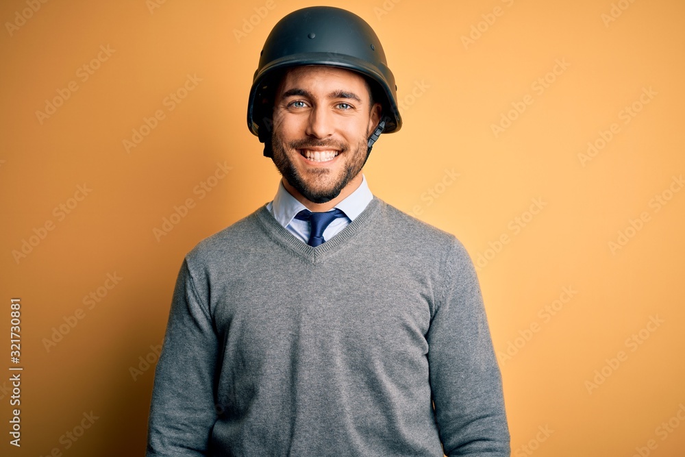 Young handsome businessman wearing military helmet over isolated yellow background with a happy and cool smile on face. Lucky person.