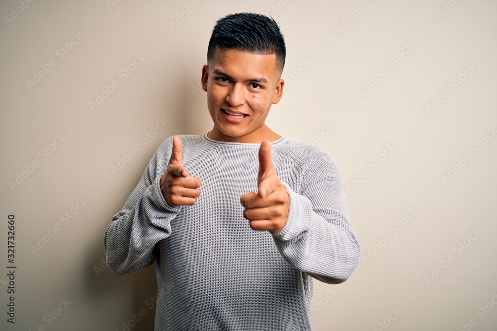 Young handsome latin man wearing casual sweater standing over isolated white background pointing fingers to camera with happy and funny face. Good energy and vibes. Young handsome latin man wearing casual sweater standing over isolated white background pointing fingers to camera with happy and funny face. Good energy and vibes.