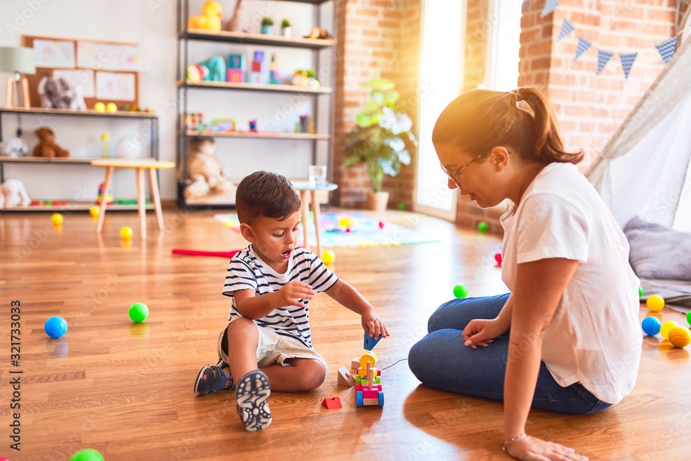 Fototapeta premium Beautiful teacher and toddler boy playing with train at kindergarten