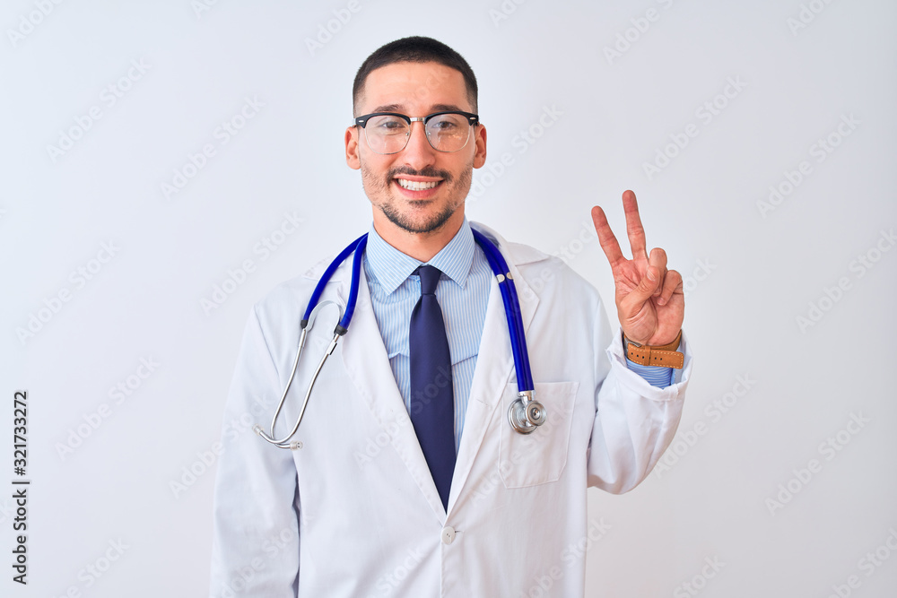 Young doctor man wearing stethoscope over isolated background showing and pointing up with fingers number two while smiling confident and happy. Young doctor man wearing stethoscope over isolated background showing and pointing up with fingers number two while smiling confident and happy.