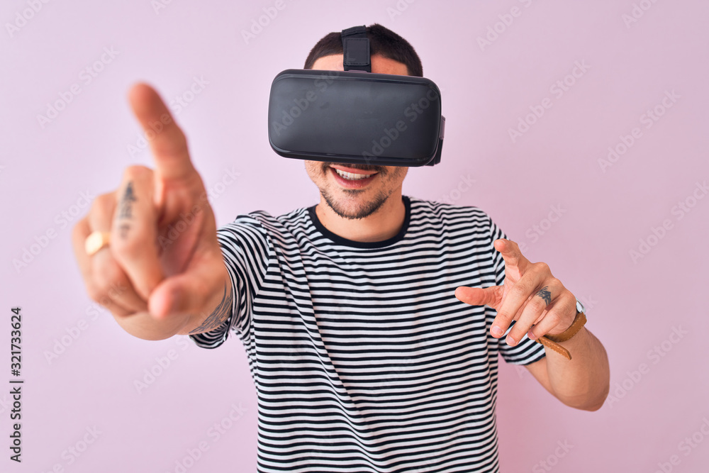 Young man playing video game wearing virtual reality glasses, looking at virtual simulation amazed and smiling happy Young man playing video game wearing virtual reality glasses, looking at virtual simulation amazed and smiling happy