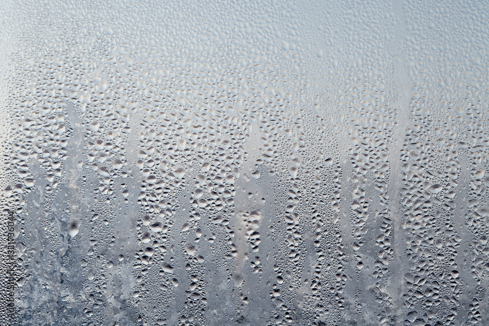 Frozen drops of condensed steam water drops on the transparent window glass.  Clean background. Condensation of moisture at extreme temperatures. Water  vapor condenses on cold window glass and freezes foto de Stock