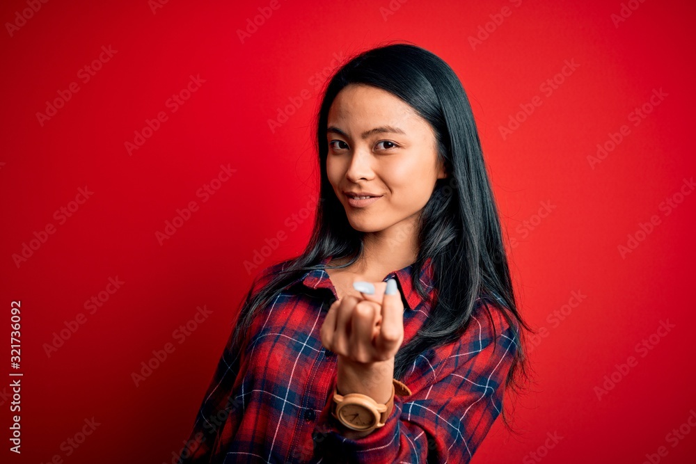 Young beautiful chinese woman wearing casual shirt over isolated red background Beckoning come here gesture with hand inviting welcoming happy and smiling Young beautiful chinese woman wearing casual shirt over isolated red background Beckoning come here gesture with hand inviting welcoming happy and smiling
