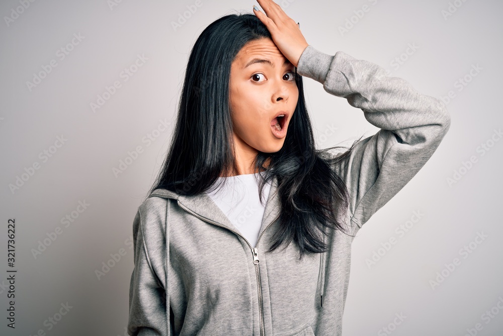 Young beautiful chinese sporty woman wearing sweatshirt over isolated white background surprised with hand on head for mistake, remember error. Forgot, bad memory concept. Young beautiful chinese sporty woman wearing sweatshirt over isolated white background surprised with hand on head for mistake, remember error. Forgot, bad memory concept.