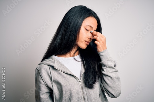 Young beautiful chinese sporty woman wearing sweatshirt over isolated white background tired rubbing nose and eyes feeling fatigue and headache. Stress and frustration concept.