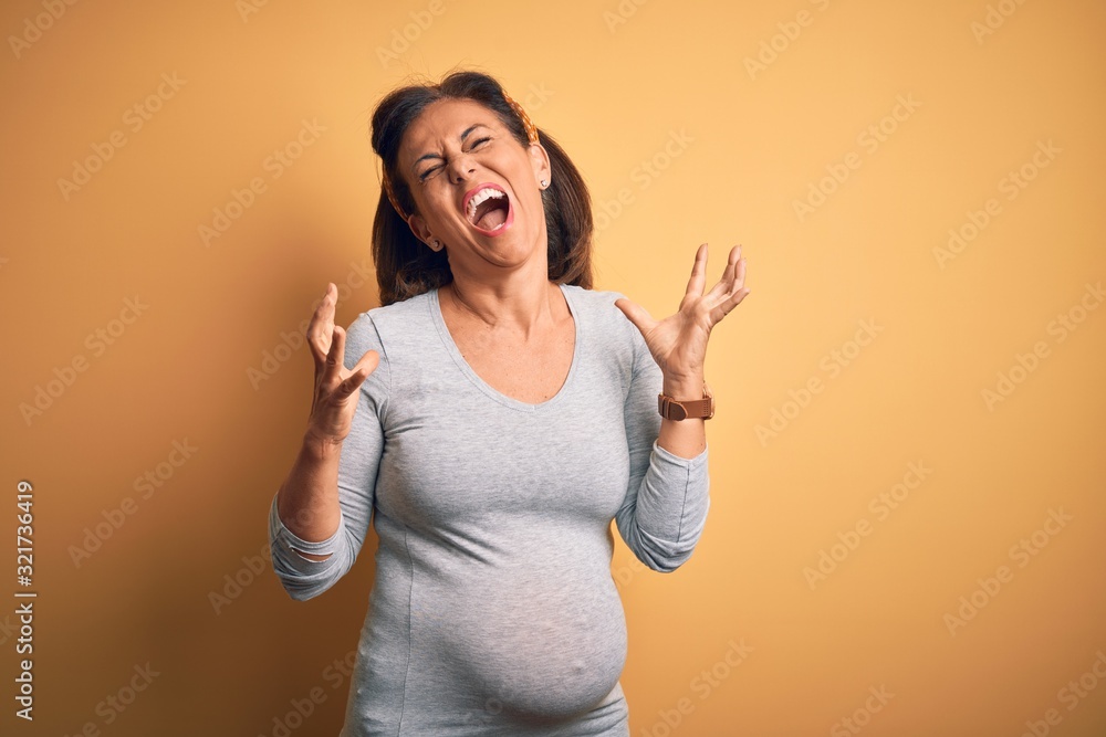 Middle age pregnant woman expecting baby at aged pregnancy crazy and mad shouting and yelling with aggressive expression and arms raised. Frustration concept. Middle age pregnant woman expecting baby at aged pregnancy crazy and mad shouting and yelling with aggressive expression and arms raised. Frustration concept.