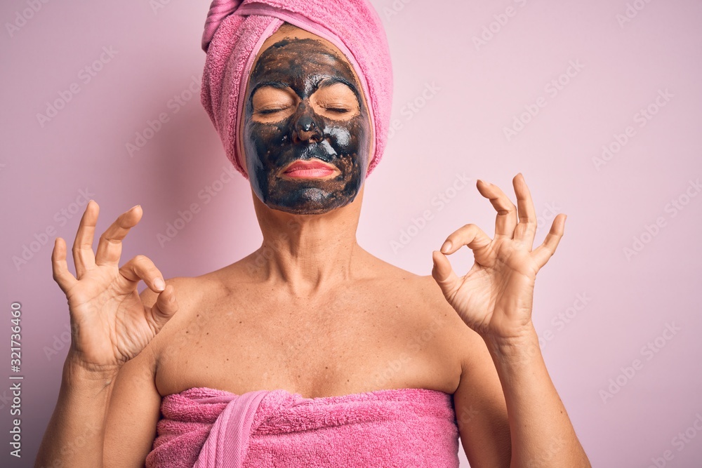 Middle age brunette woman wearing beauty black face mask over isolated pink background relaxed and smiling with eyes closed doing meditation gesture with fingers. Yoga concept. Middle age brunette woman wearing beauty black face mask over isolated pink background relaxed and smiling with eyes closed doing meditation gesture with fingers. Yoga concept.