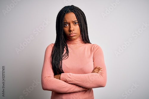 Young african american woman standing casual and cool over white isolated background skeptic and nervous, disapproving expression on face with crossed arms. Negative person.