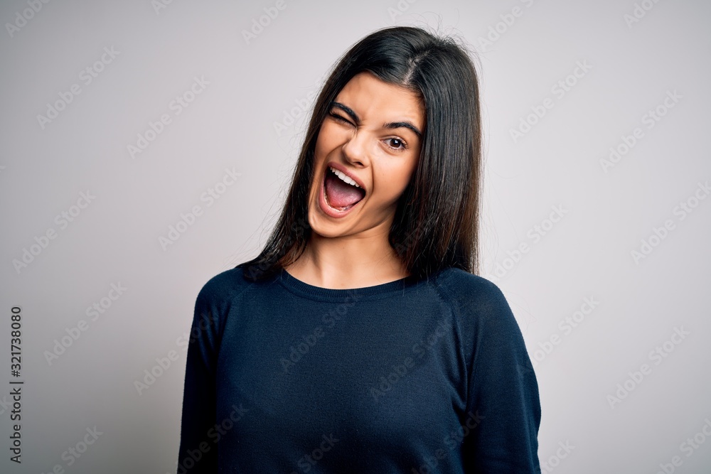 Young beautiful brunette woman wearing casual sweater standing over white background winking looking at the camera with sexy expression, cheerful and happy face. Young beautiful brunette woman wearing casual sweater standing over white background winking looking at the camera with sexy expression, cheerful and happy face.