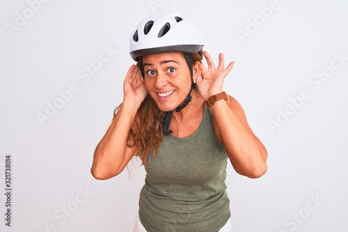 Middle age mature cyclist woman wearing safety helmet over isolated background Trying to hear both hands on ear gesture, curious for gossip. Hearing problem, deaf