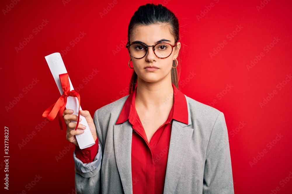 Young beautiful brunette student woman wearing glasses holding university degree diploma with a confident expression on smart face thinking serious Young beautiful brunette student woman wearing glasses holding university degree diploma with a confident expression on smart face thinking serious
