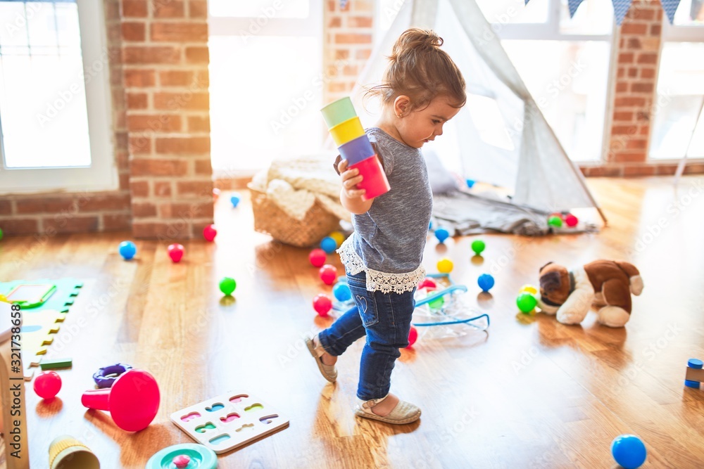 Beautiful toddler standing playing with colorful plastic cups at kindergarten - obrazy, fototapety, plakaty 