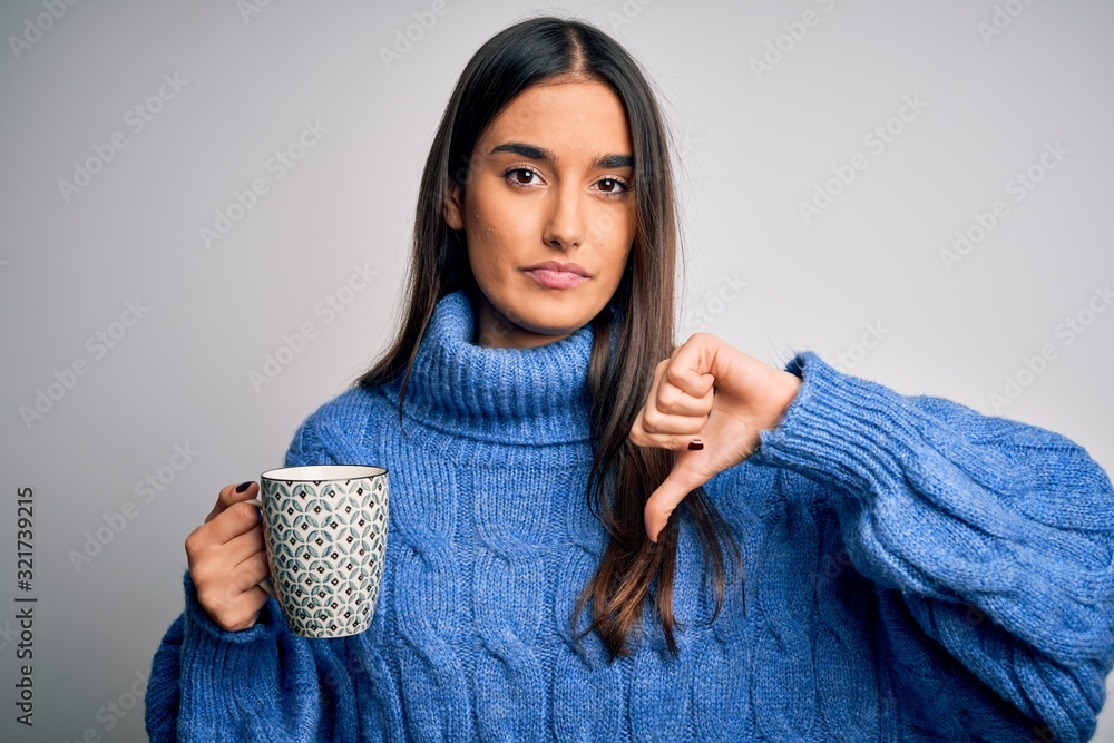 Young beautiful brunette woman drinking cup of coffee over isolated white background with angry face, negative sign showing dislike with thumbs down, rejection concept Young beautiful brunette woman drinking cup of coffee over isolated white background with angry face, negative sign showing dislike with thumbs down, rejection concept