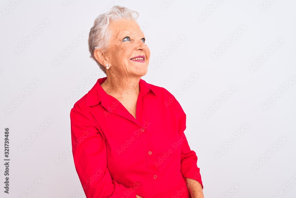 Senior grey-haired woman wearing red casual shirt standing over isolated white background looking away to side with smile on face, natural expression. Laughing confident. Senior grey-haired woman wearing red casual shirt standing over isolated white background looking away to side with smile on face, natural expression. Laughing confident.