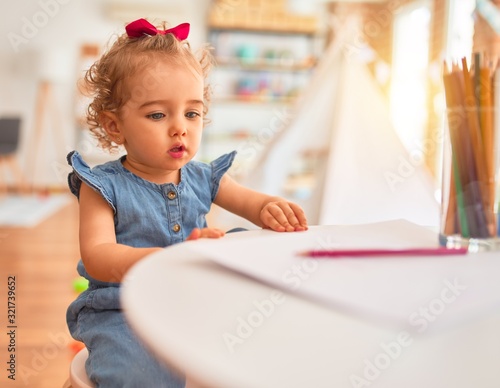 Beautiful caucasian infant playing with toys at colorful playroom. Happy and playful drawing with color pencils at kindergarten.