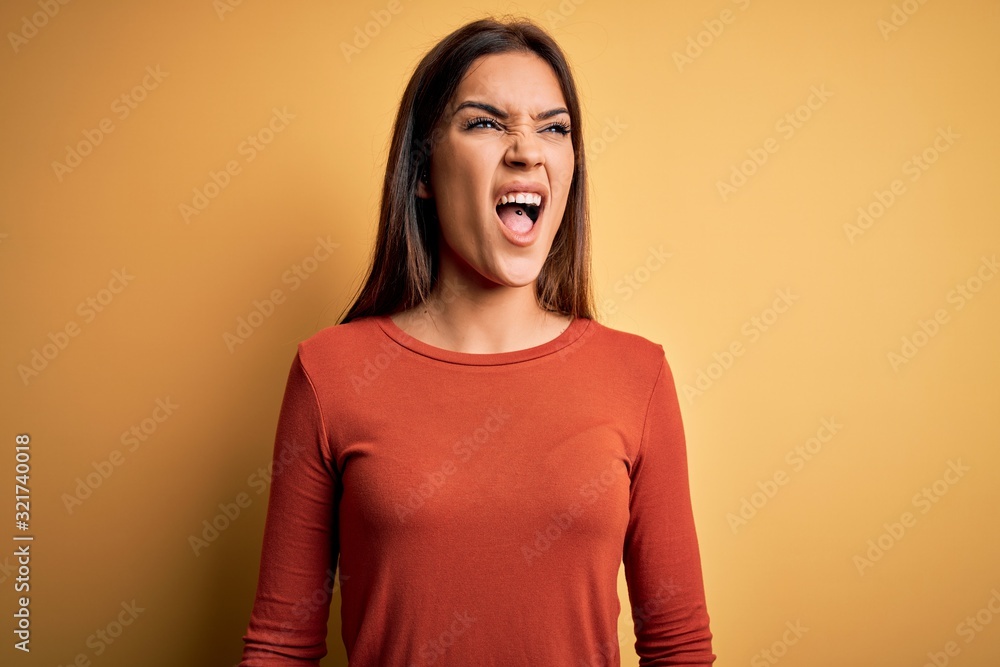 Young beautiful brunette woman wearing casual t-shirt standing over yellow background angry and mad screaming frustrated and furious, shouting with anger. Rage and aggressive concept. Young beautiful brunette woman wearing casual t-shirt standing over yellow background angry and mad screaming frustrated and furious, shouting with anger. Rage and aggressive concept.