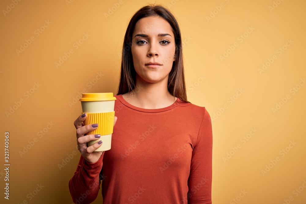 Young beautiful brunette woman drinking cup of takeaway coffe over yellow background with a confident expression on smart face thinking serious Young beautiful brunette woman drinking cup of takeaway coffe over yellow background with a confident expression on smart face thinking serious