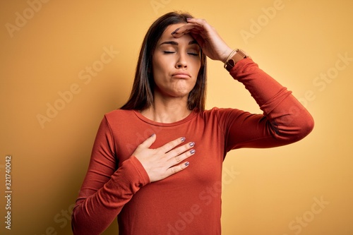 Young beautiful brunette woman wearing casual t-shirt standing over yellow background Touching forehead for illness and fever, flu and cold, virus sick © Krakenimages.com