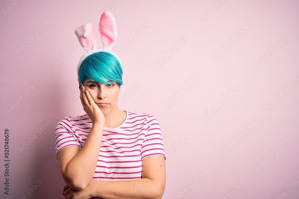 Young woman with fashion blue hair wearing easter rabbit ears over pink background thinking looking tired and bored with depression problems with crossed arms. Young woman with fashion blue hair wearing easter rabbit ears over pink background thinking looking tired and bored with depression problems with crossed arms.