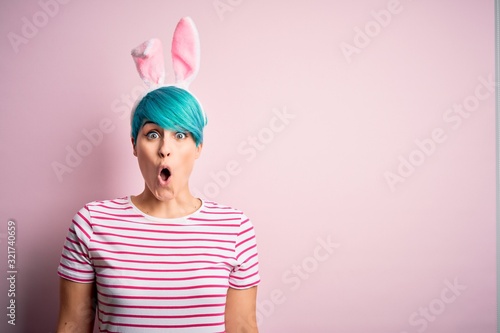 Photography Young woman with fashion blue hair wearing easter rabbit ears over pink background afraid and shocked with surprise expression, fear and excited face