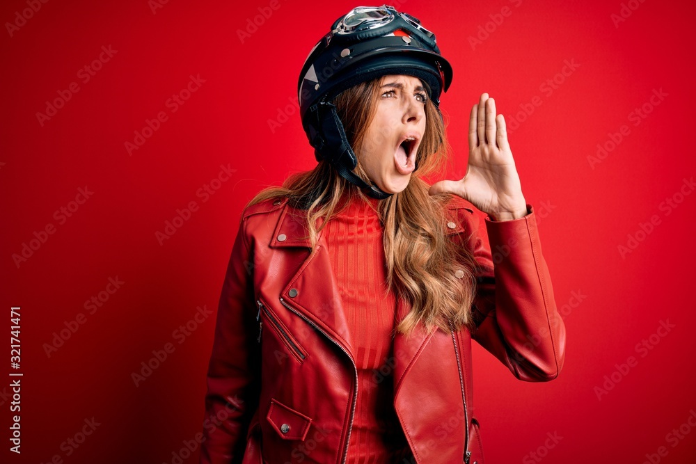 Young beautiful brunette motrocyclist woman wearing moto helmet over red background shouting and screaming loud to side with hand on mouth. Communication concept. Young beautiful brunette motrocyclist woman wearing moto helmet over red background shouting and screaming loud to side with hand on mouth. Communication concept.