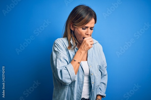 Middle age beautiful woman wearing casual shirt standing over isolated blue background feeling unwell and coughing as symptom for cold or bronchitis. Health care concept.