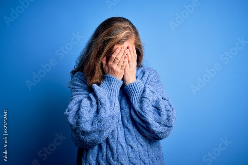Young beautiful blonde woman wearing casual turtleneck sweater over blue background with sad expression covering face with hands while crying. Depression concept.