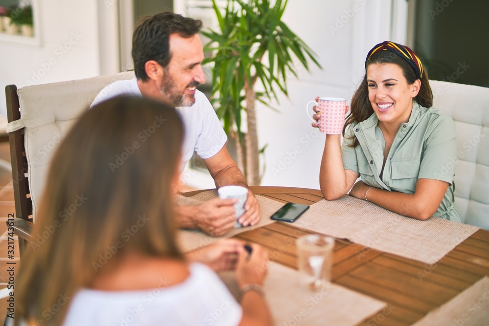 Fototapeta premium Beautiful family sitting on terrace drinking cup of coffee speaking and smiling