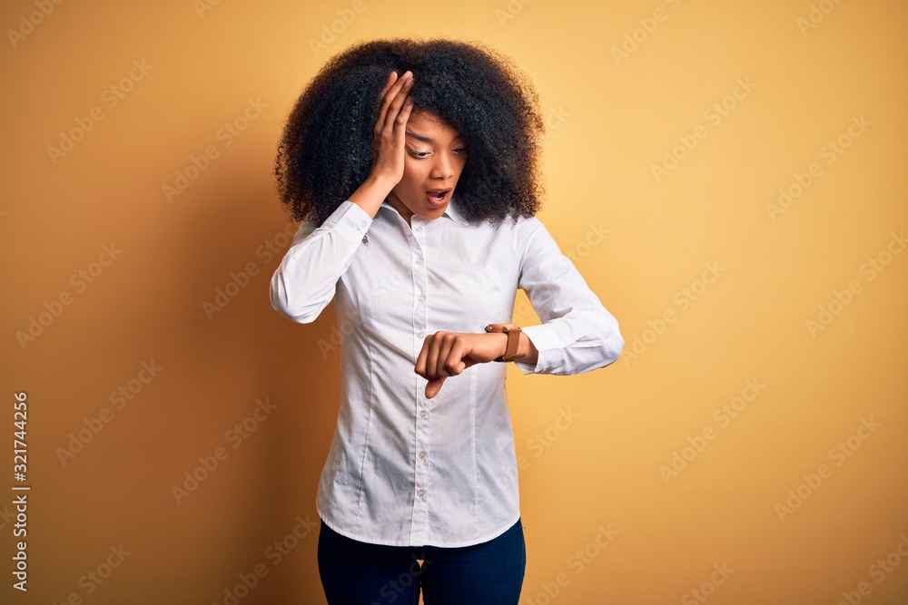 Young beautiful african american elegant woman with afro hair standing over yellow background Looking at the watch time worried, afraid of getting late Young beautiful african american elegant woman with afro hair standing over yellow background Looking at the watch time worried, afraid of getting late