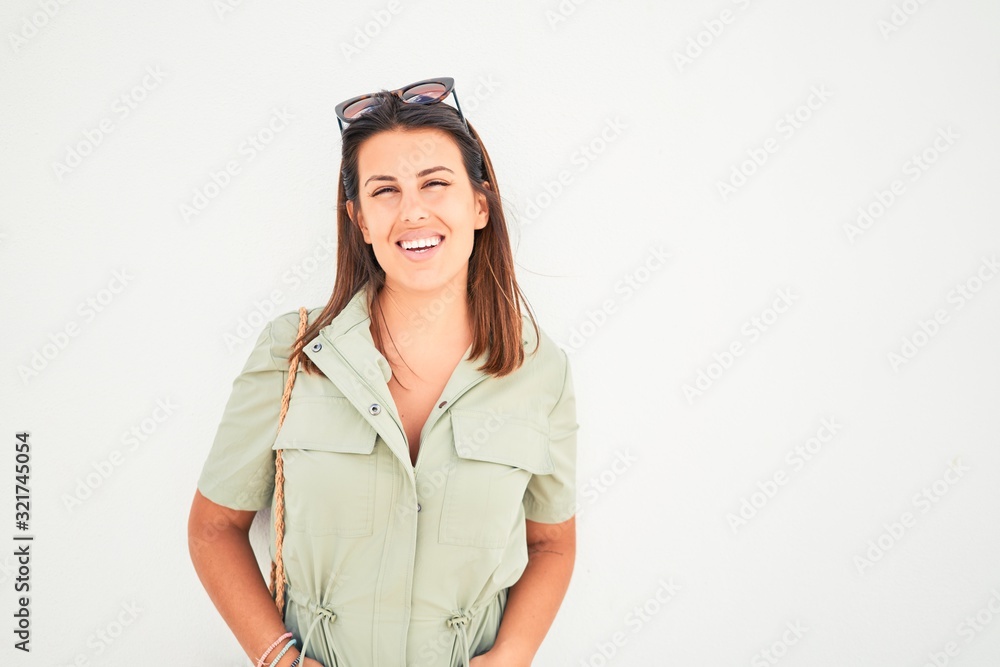 Beautiful girl leaning on white wall, young friendly woman smiling happy on a sunny day of summer Beautiful girl leaning on white wall, young friendly woman smiling happy on a sunny day of summer