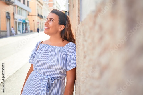 Young beautiful woman smiling happy leaning on the wall of city streets on a sunny day of summer