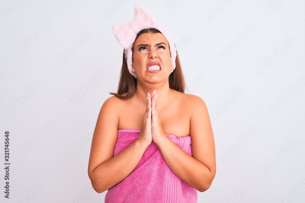 Beautiful young woman wearing pink shower towel and beauty headband over white background begging and praying with hands together with hope expression on face very emotional and worried. Asking Beautiful young woman wearing pink shower towel and beauty headband over white background begging and praying with hands together with hope expression on face very emotional and worried. Asking