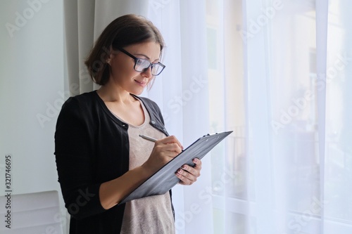 Mature woman couch taking notes standing near window in office photo
